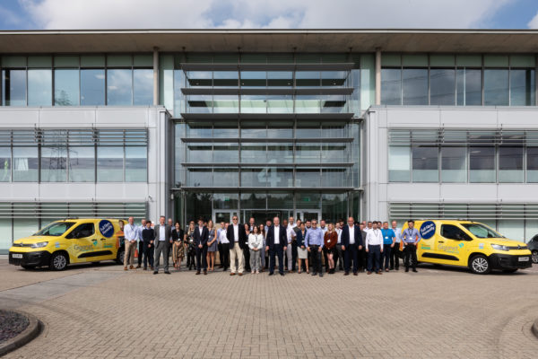 Giganet staff stood outside office with yellow Giganet broadband vans to the left and right.