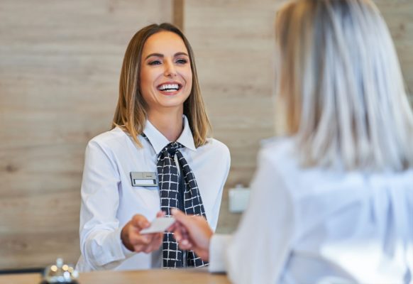 Hospitality staff member smiling at front desk while handing customer hotel room card