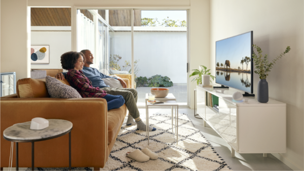 Women and man sat on orange sofa watching tv via giganet broadband in a white decorated room